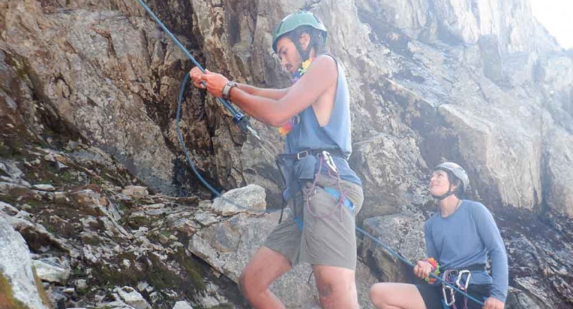 a gap year student belays a climber while another looks on during the rock climbing portion of an outdoor educator course with outward bound